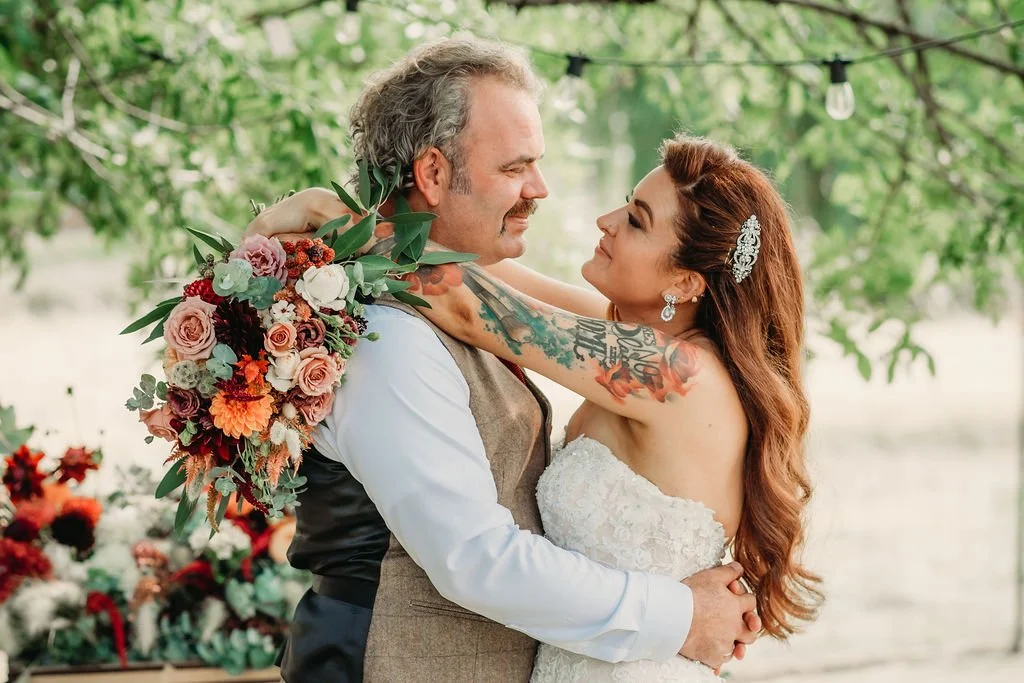 A bride and groom hugging at their outdoor wedding, with the bride holding a bridal bouquet. Photo by Cassidy Baldwin Photography