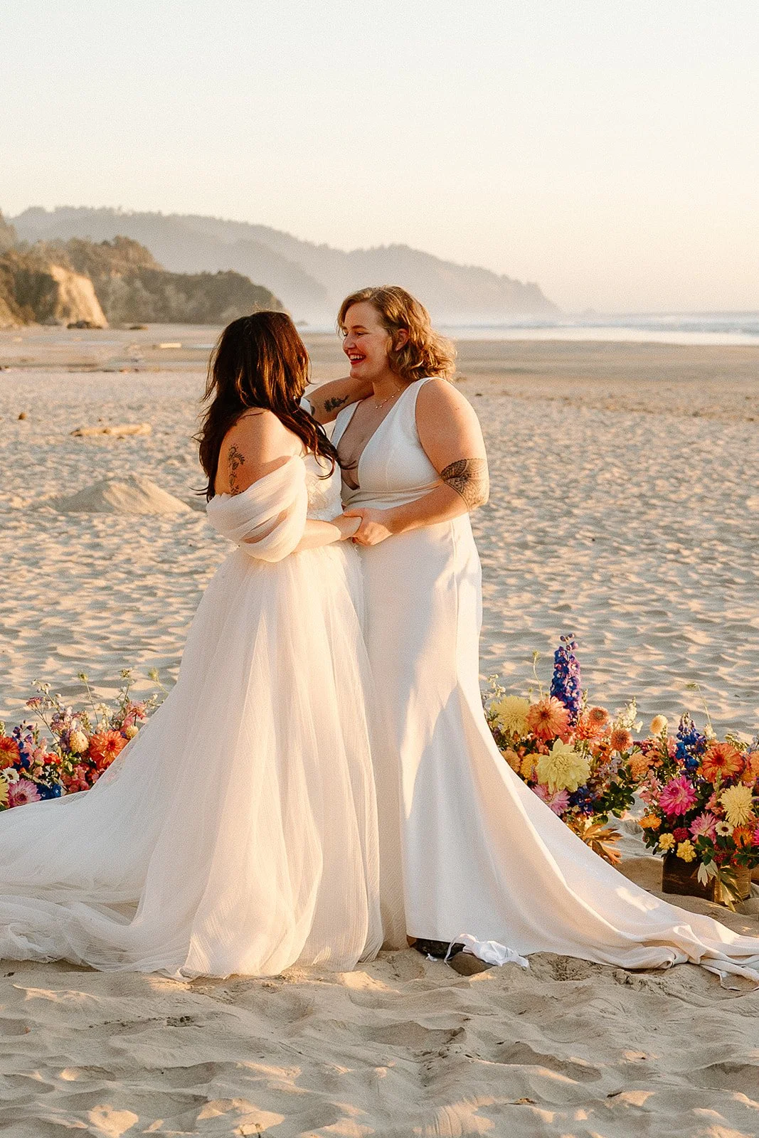 Two brides in wedding dresses smiling and holding hands on a sandy beach with colorful flowers nearby, during sunset.

Photo by Forgette Photo
Venue: the beautiful Oregon Coast