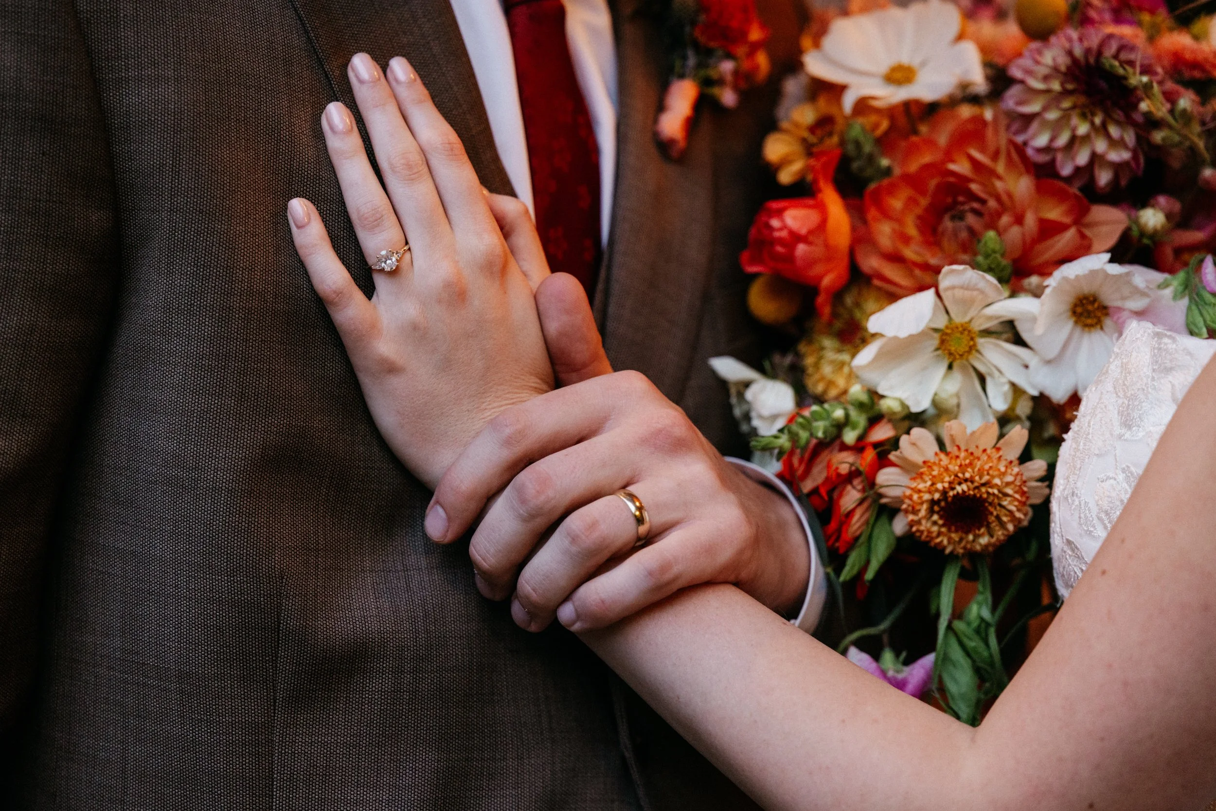 Close-up of a bride and groom holding hands, showing wedding rings, with a floral bouquet nearby.

Photo by Ivory Creek Photography
Venue: Summit Grove Lodge in Ridgefield, WA