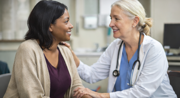 Medical professional smiling and talking with a woman in a healthcare setting.