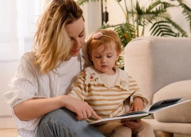 A woman reading a book with a young girl sitting on her lap in a cozy living room.