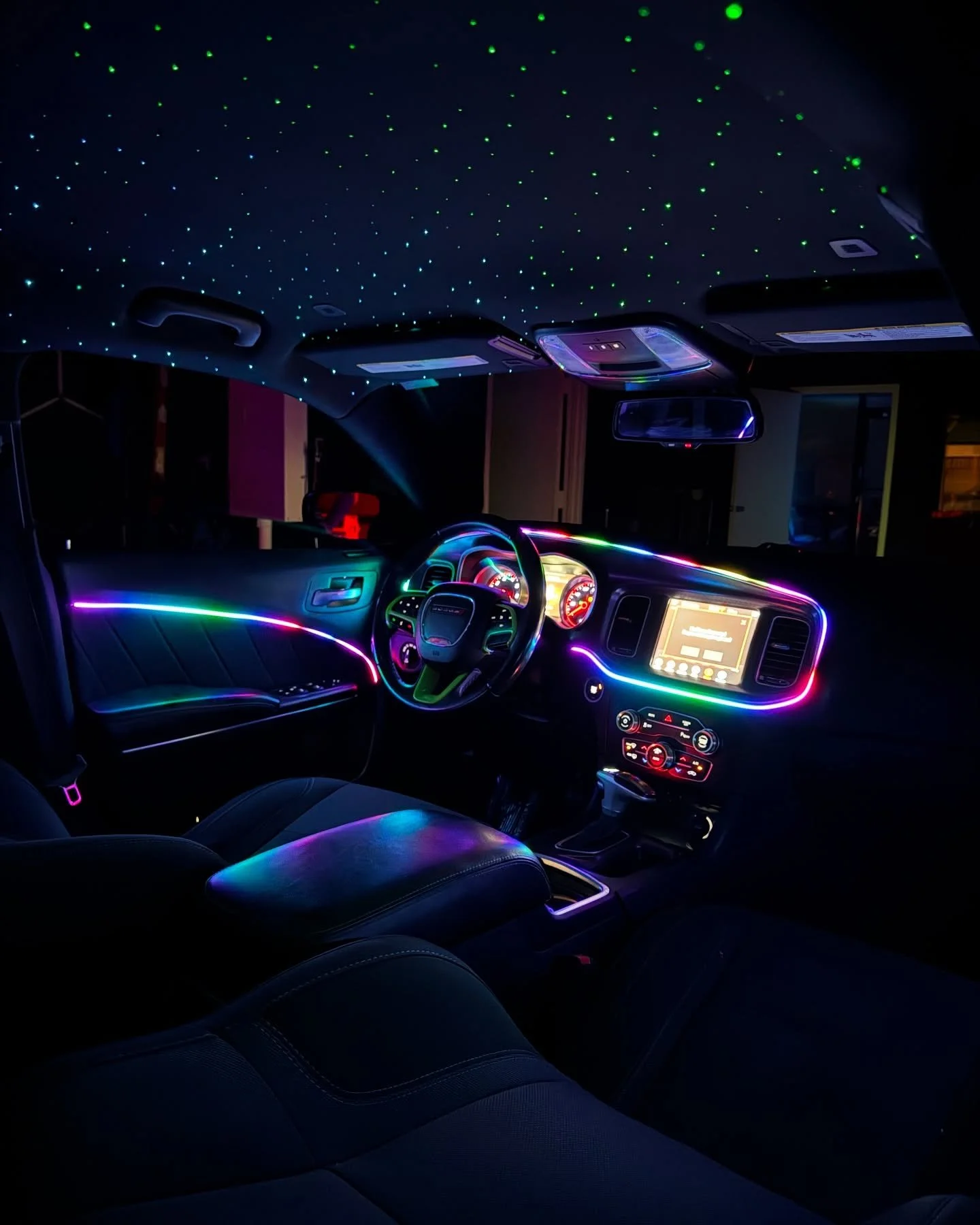 Interior of a car with neon multicolor LED lights, starry sky projection on the ceiling, illuminated dashboard, and a touchscreen display.