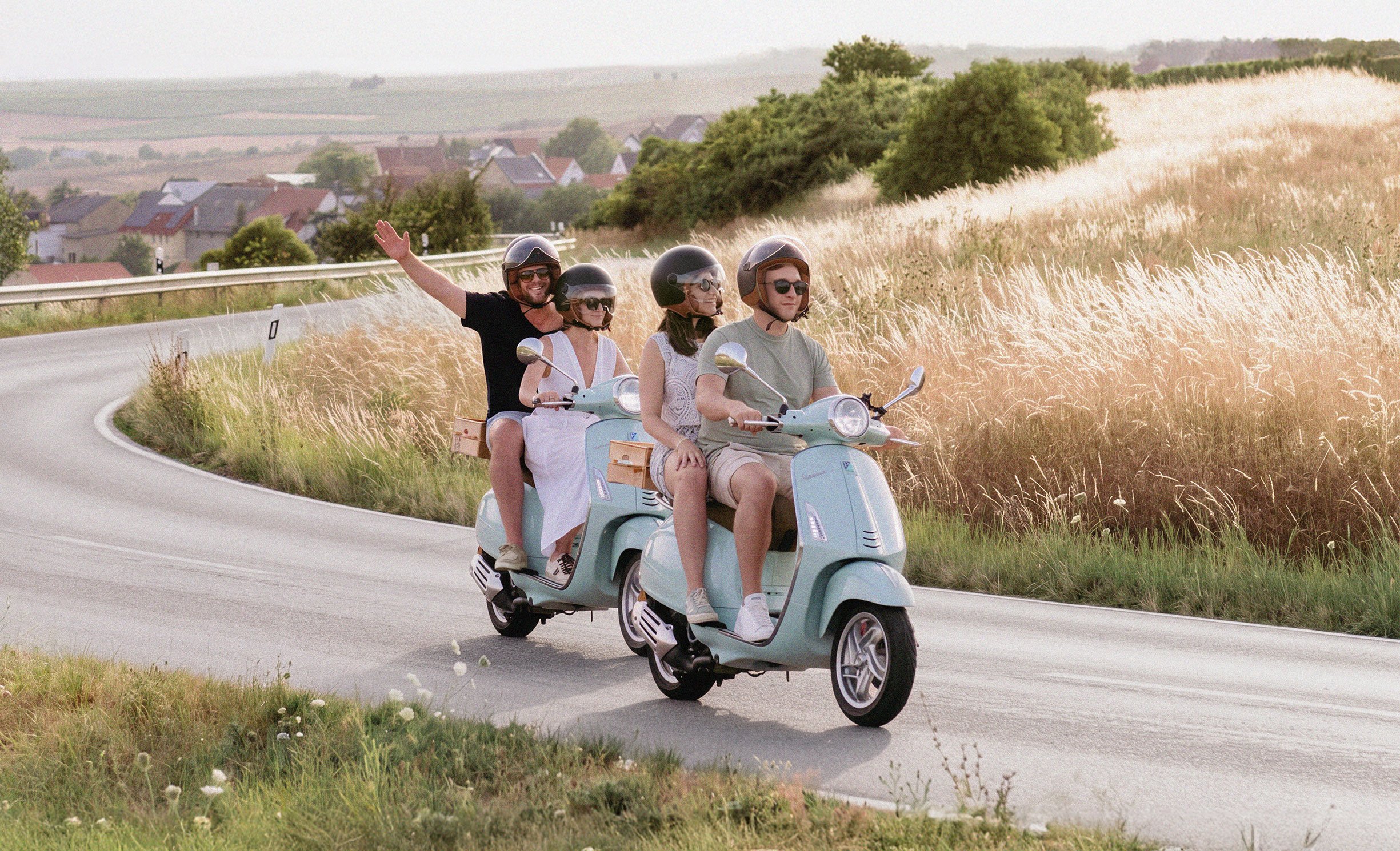 Zwei Personen auf einer Vespa winken während einer Tour durch Rheinhessen