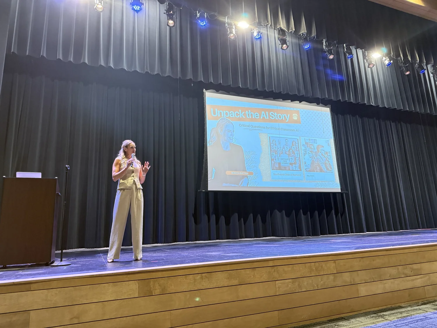 A woman on stage speaking into a microphone during a presentation titled 'Unpack the AI Story' with a slide showing illustrations and text about ethical classroom AI, at an indoor event.