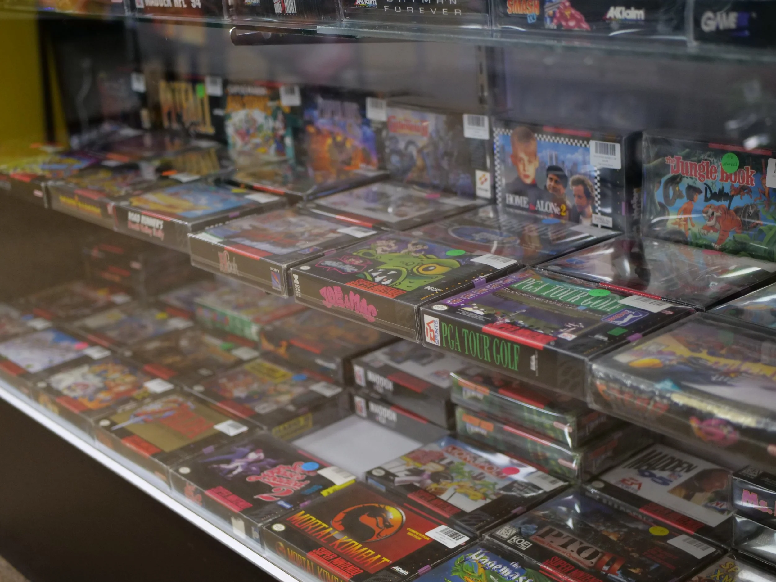 Video game cases on display in a store shelf, with titles including 'Mortal Kombat,' 'The Jungle Book,' 'PGA Tour Golf,' and 'Nightmare.'