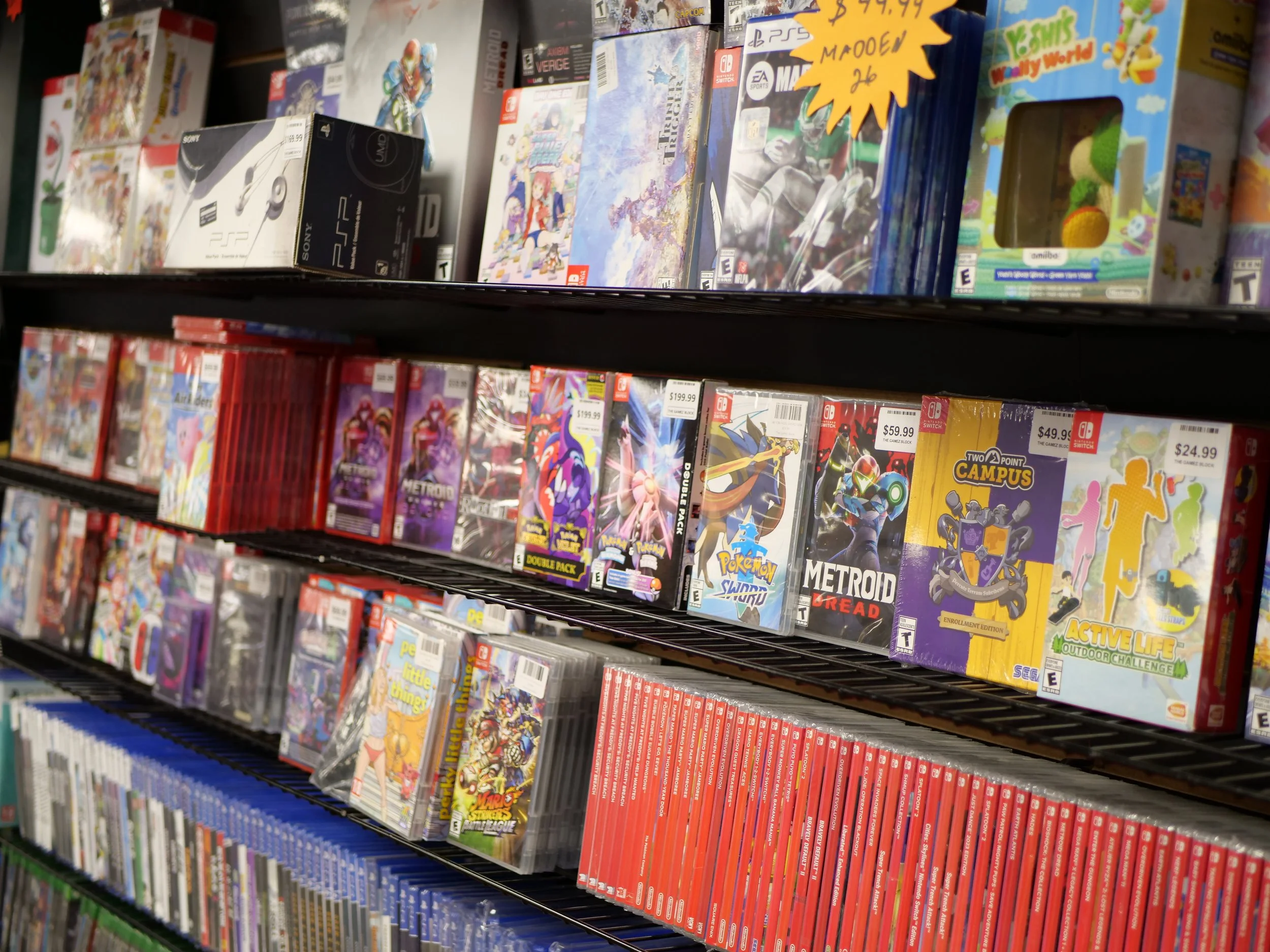 Video game cases on store shelves, including Nintendo Switch, PlayStation, and boxed games, with some promotional signs and prices visible.