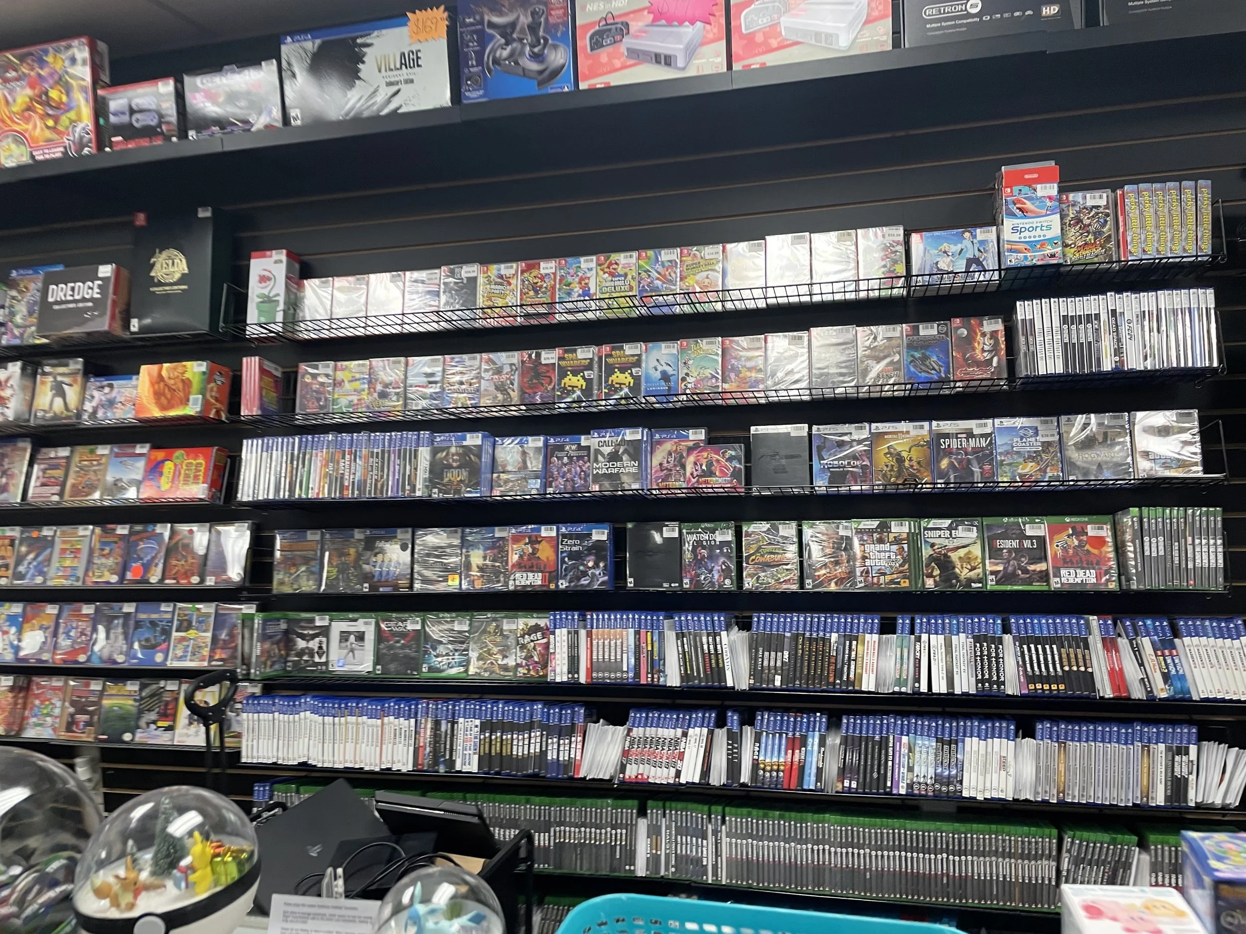 Shelf filled with video game cases in an electronics store, including popular titles like Spider-Man, Call of Duty, and Assassin's Creed.