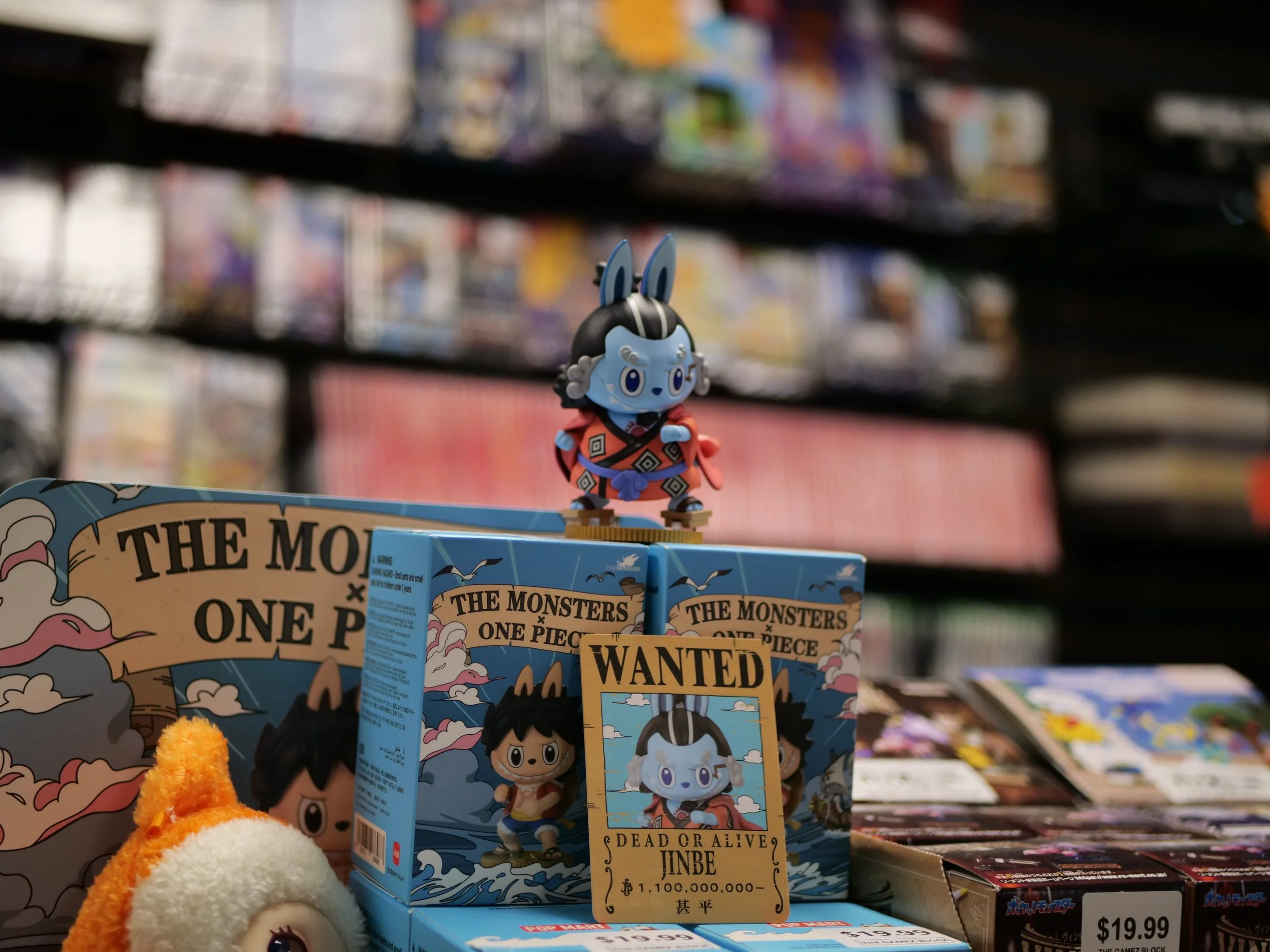 A figurine from the anime One Piece, specifically of Jinbe, is displayed on top of a blue box with other One Piece merchandise and promotional signs, in a store aisle with shelves filled with various boxed items in the background.