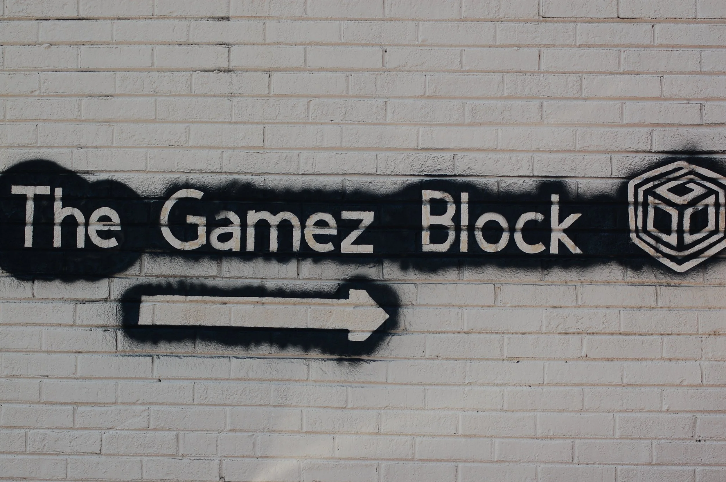 Graffiti on a brick wall with the text 'The Gamez Block' and a right arrow, along with a cube logo.
