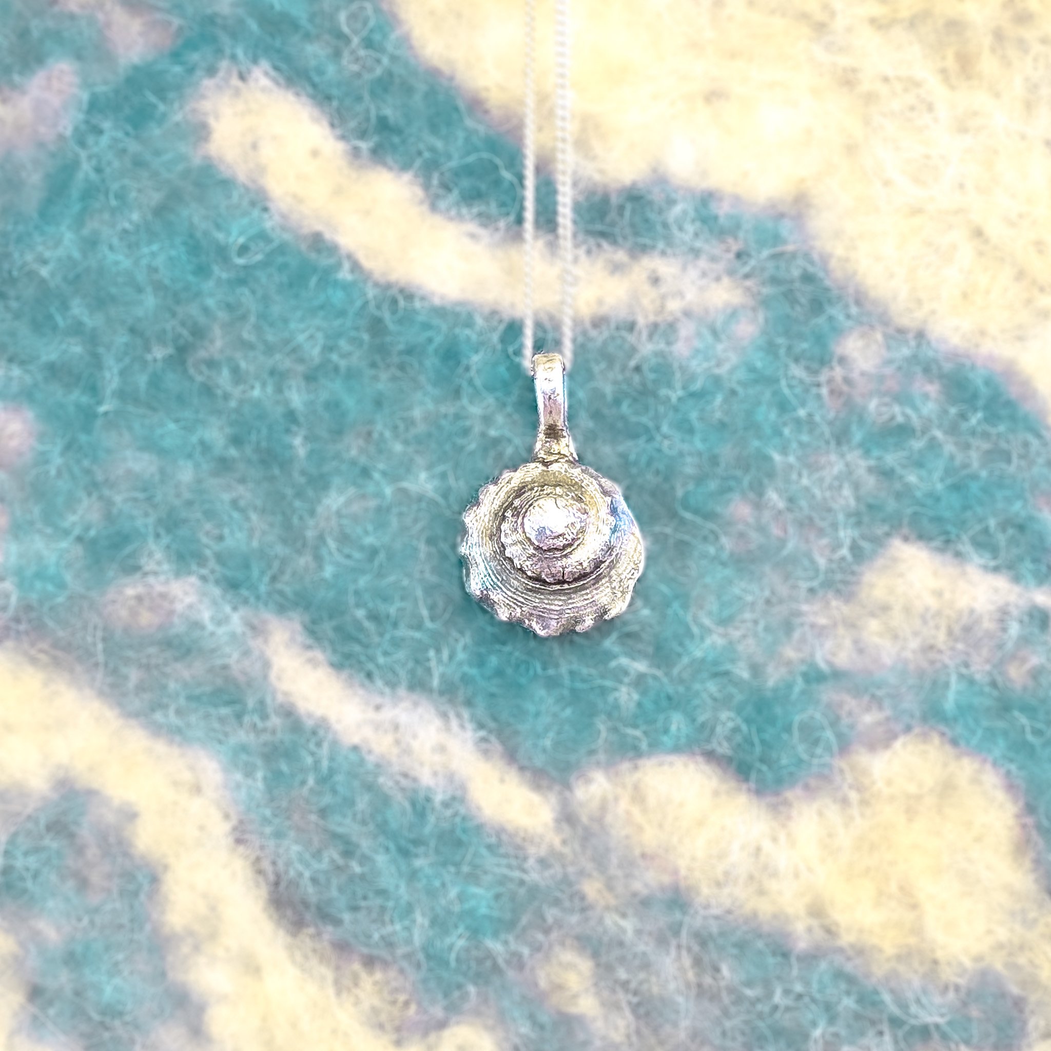 Fine silver textured shell pendant with concentric ridged rings, worn on a silver chain against bare skin