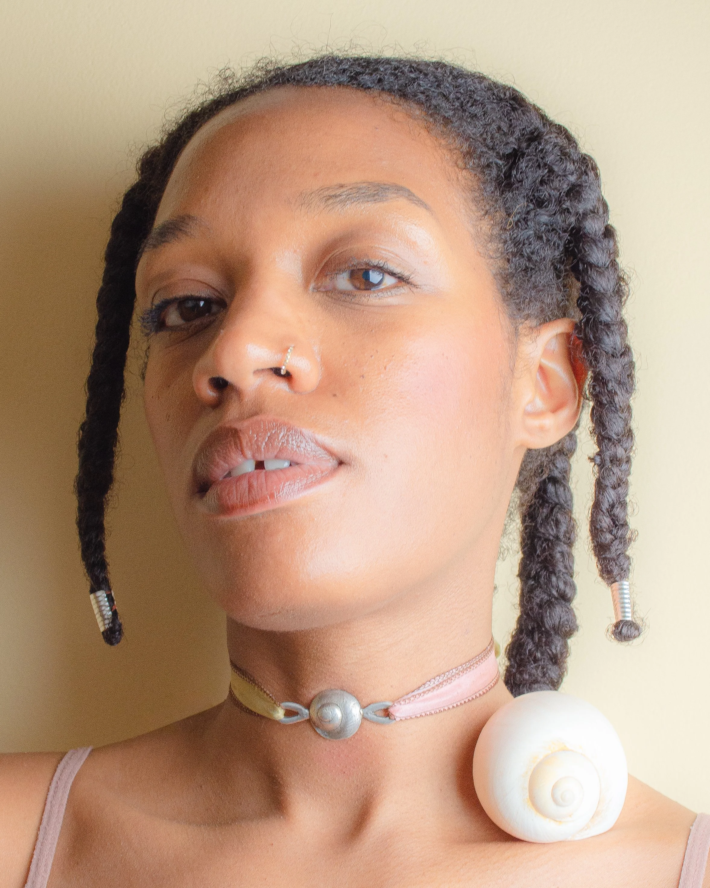 Fine silver round shell pendant on a silk ribbon, worn against bare skin, with a large white scallop shell in the background