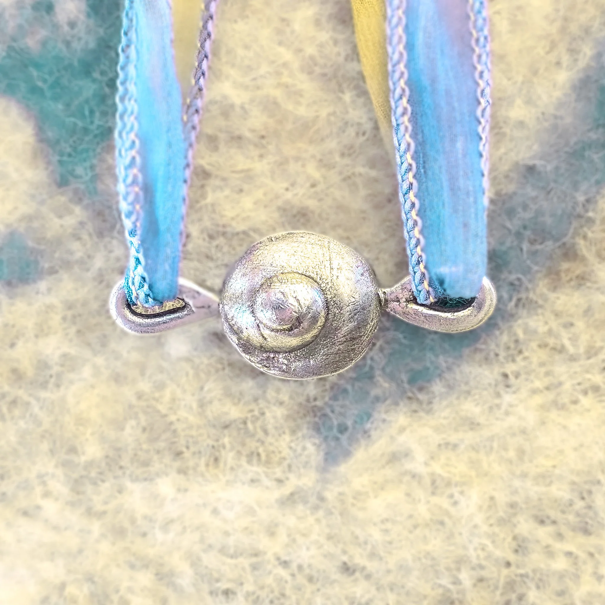 Fine silver round shell pendant on a silk ribbon, worn against bare skin, with a large white scallop shell in the background