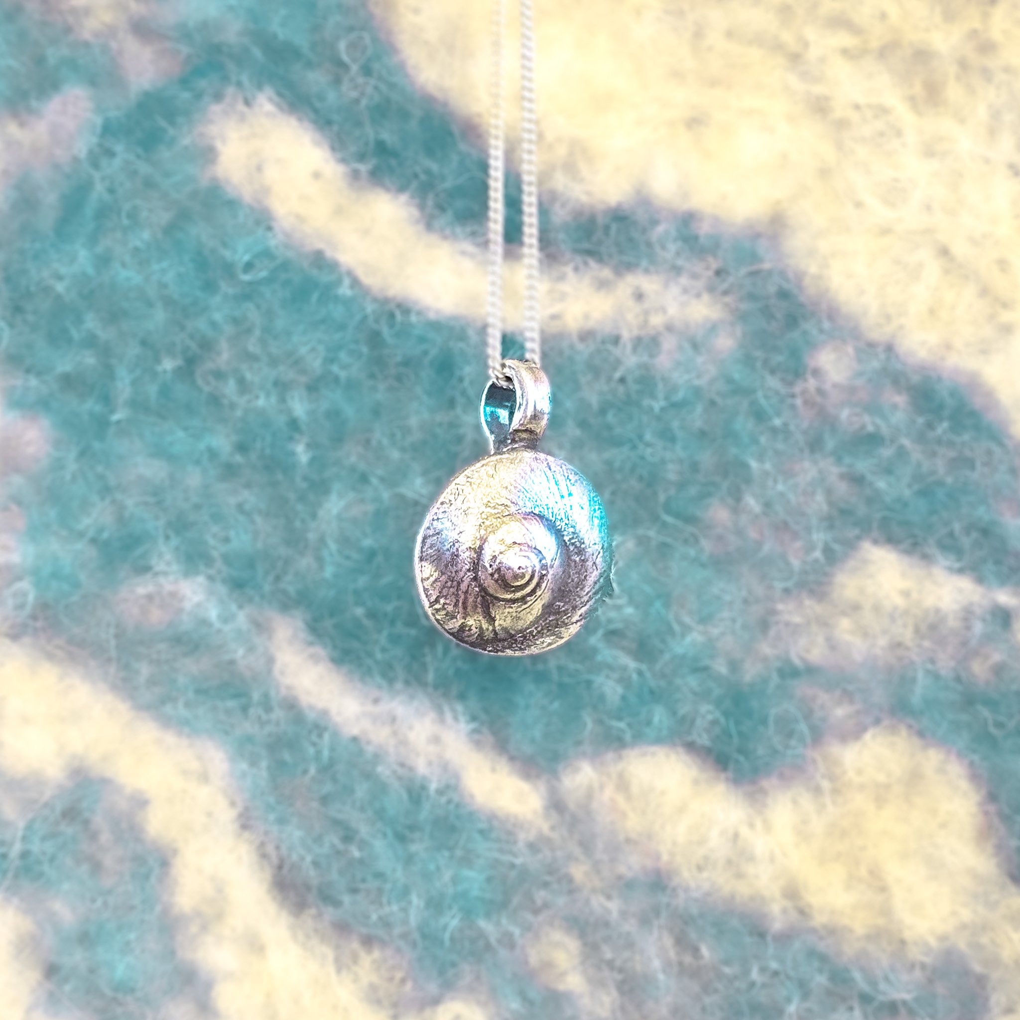 Fine silver round shell pendant on a silver chain, worn against bare skin, with a large white scallop shell in the background