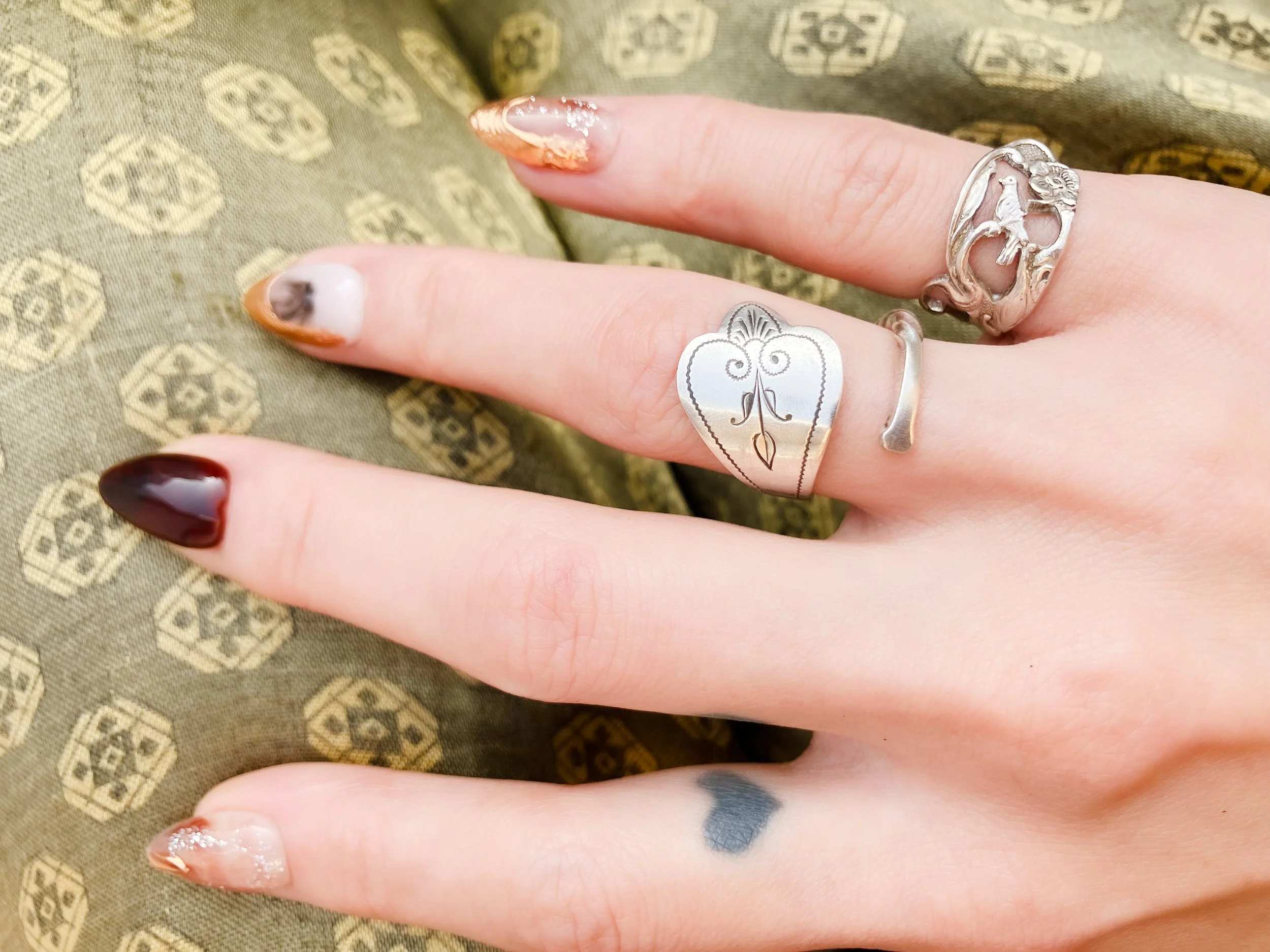 Vintage Dutch 925 sterling silver rings made from fork handles with openwork songbird and floral motif, handmade by Moonlit Manor Netherlands, on human hand against an olive sheen green background