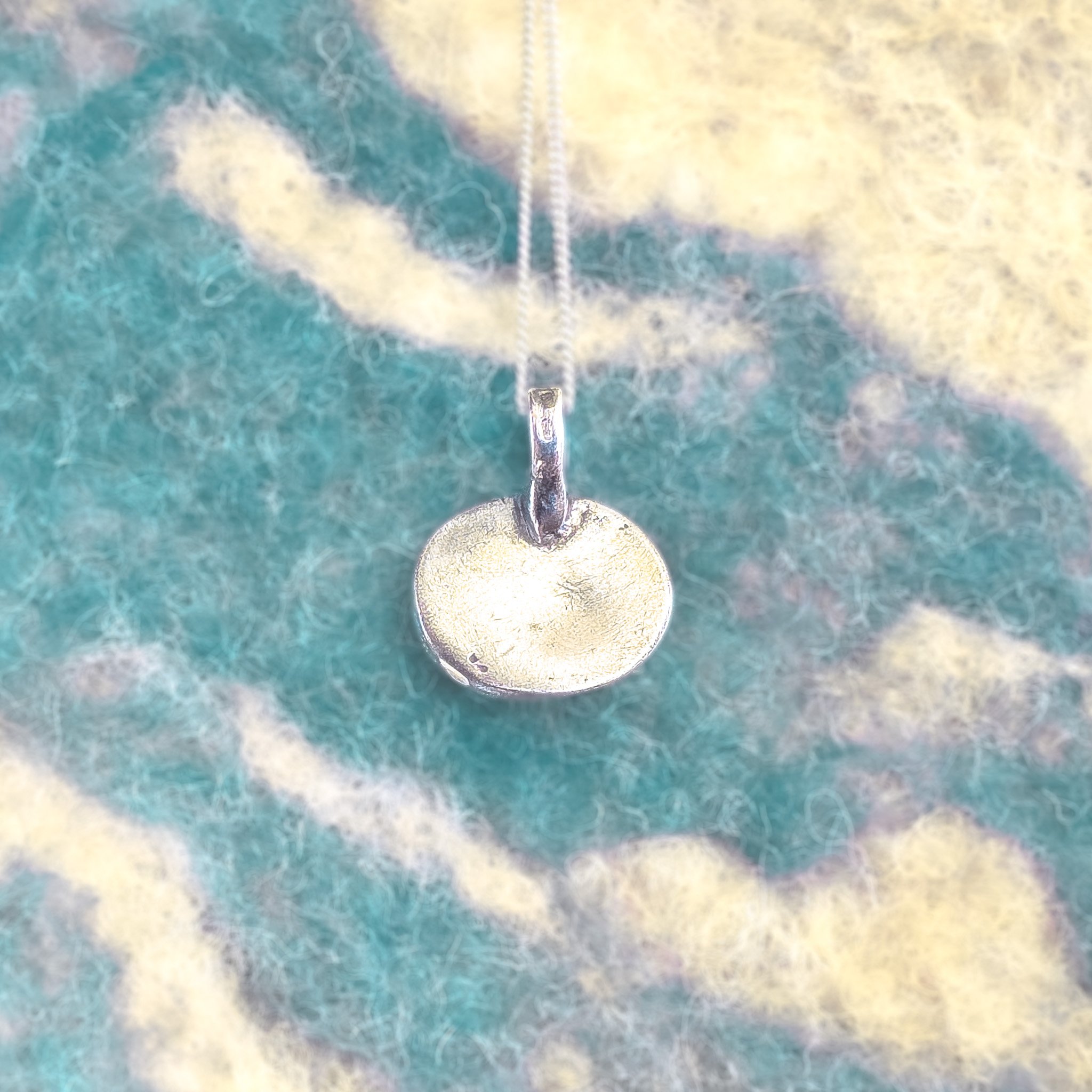 Fine silver round shell pendant on a silver chain, worn against bare skin, with a large white scallop shell in the background