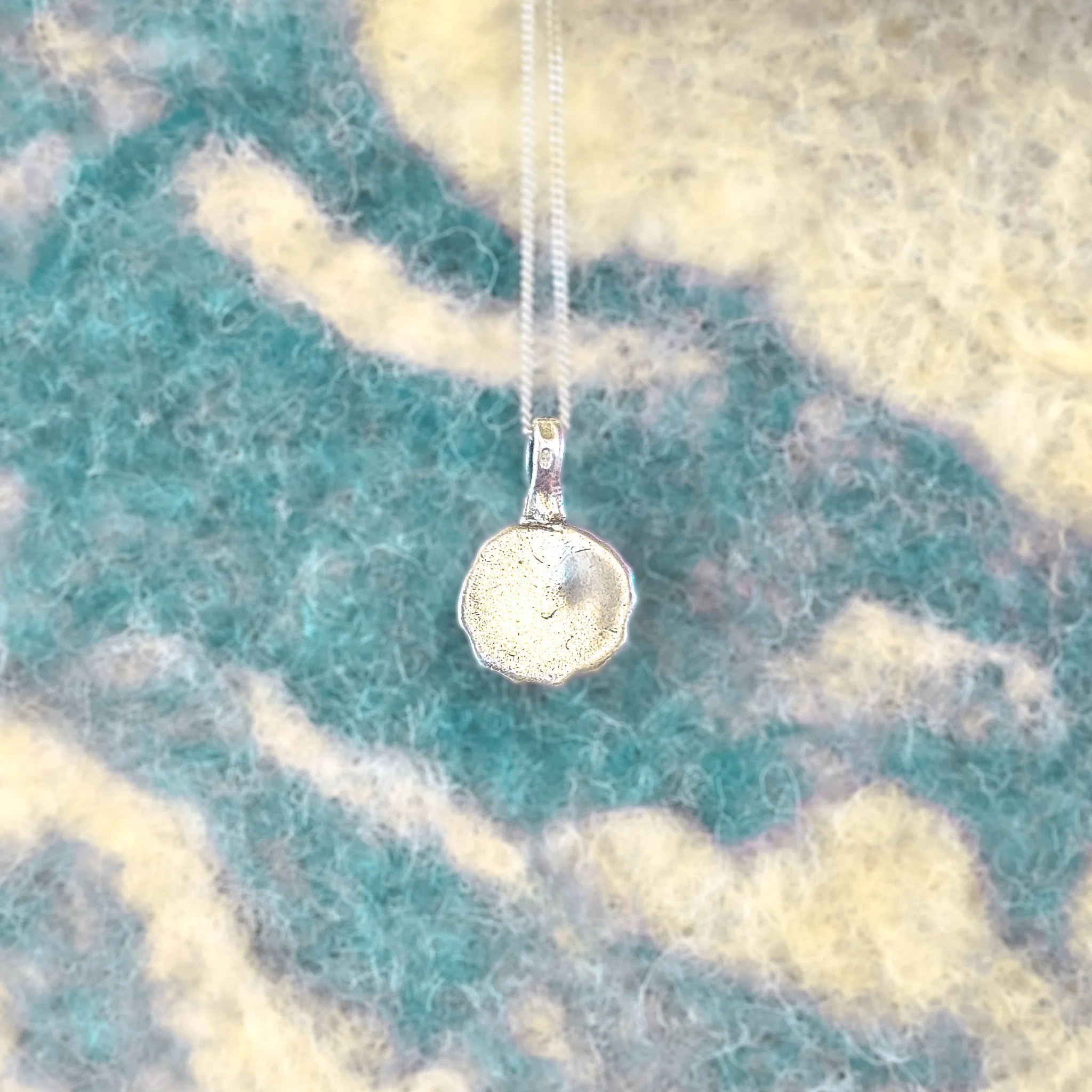 Fine silver textured shell pendant with concentric ridged rings, worn on a silver chain against bare skin
