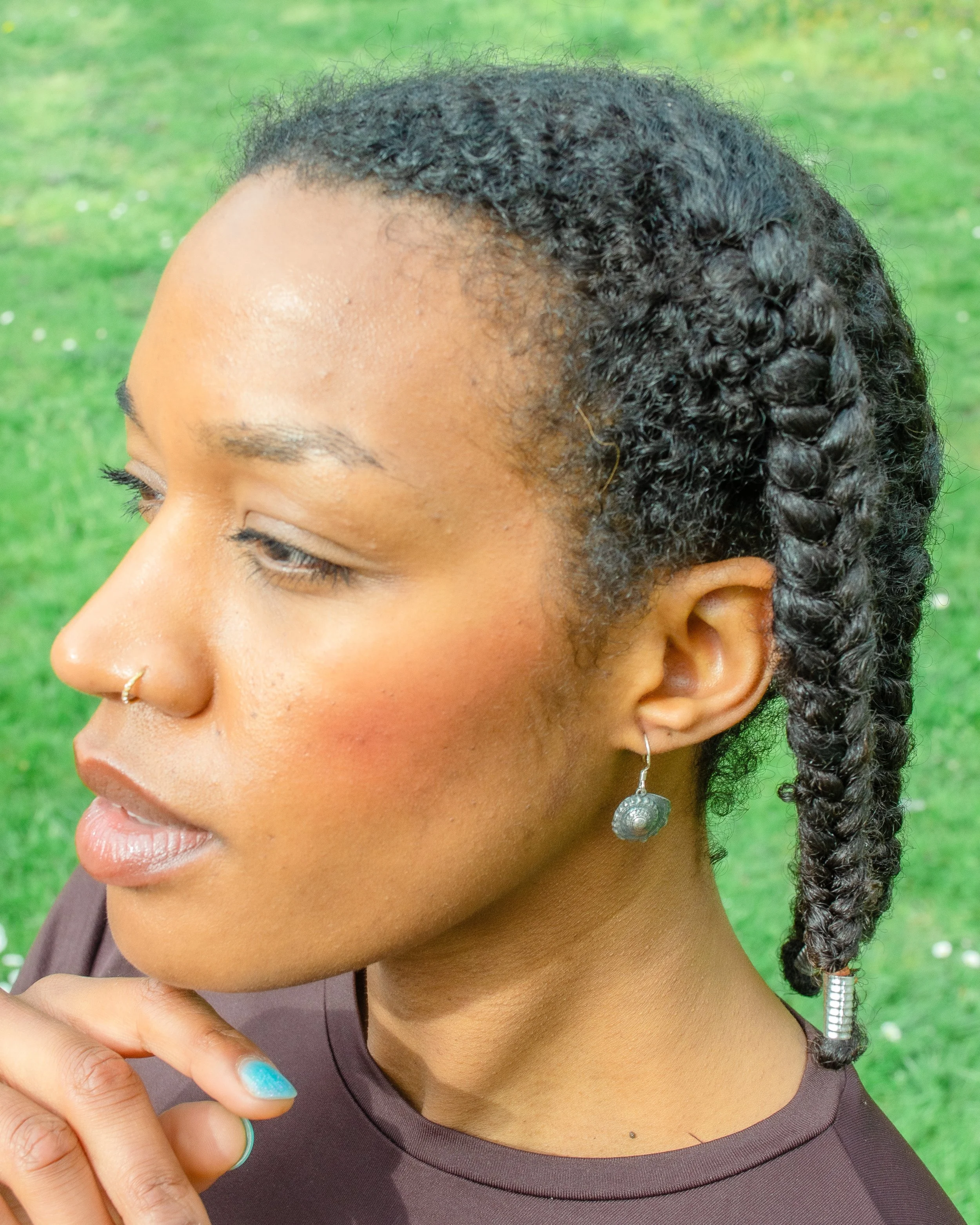 Fine silver round shell earring worn against bare skin, with a large grey scallop shell in the background