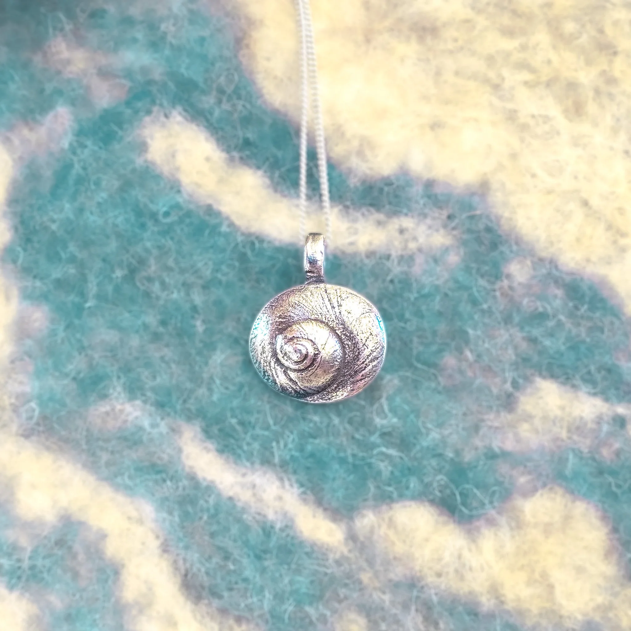 Fine silver round shell pendant on a silver chain, worn against bare skin, with a large white scallop shell in the background