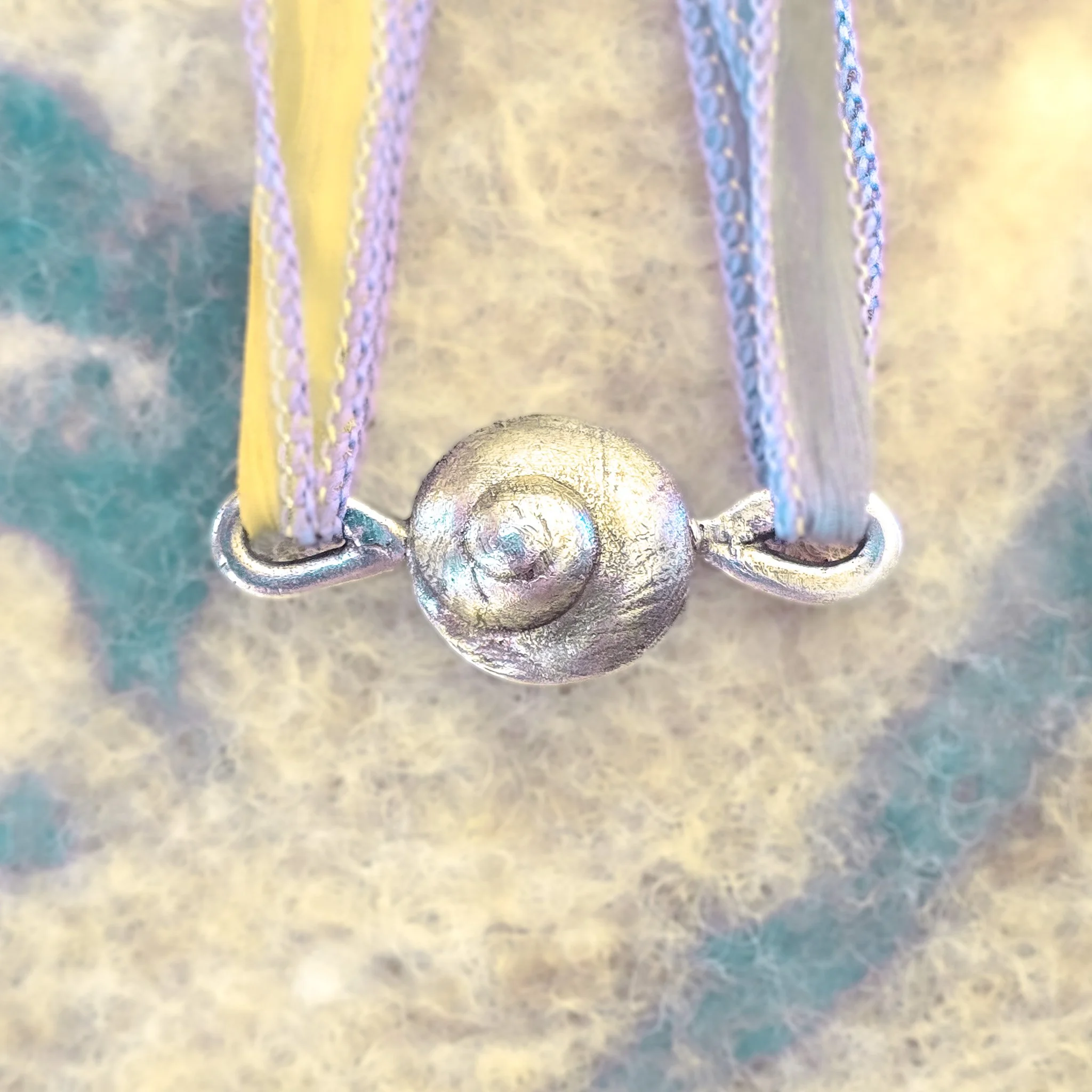 Fine silver round shell pendant on a silk ribbon, worn against bare skin, with a large white scallop shell in the background