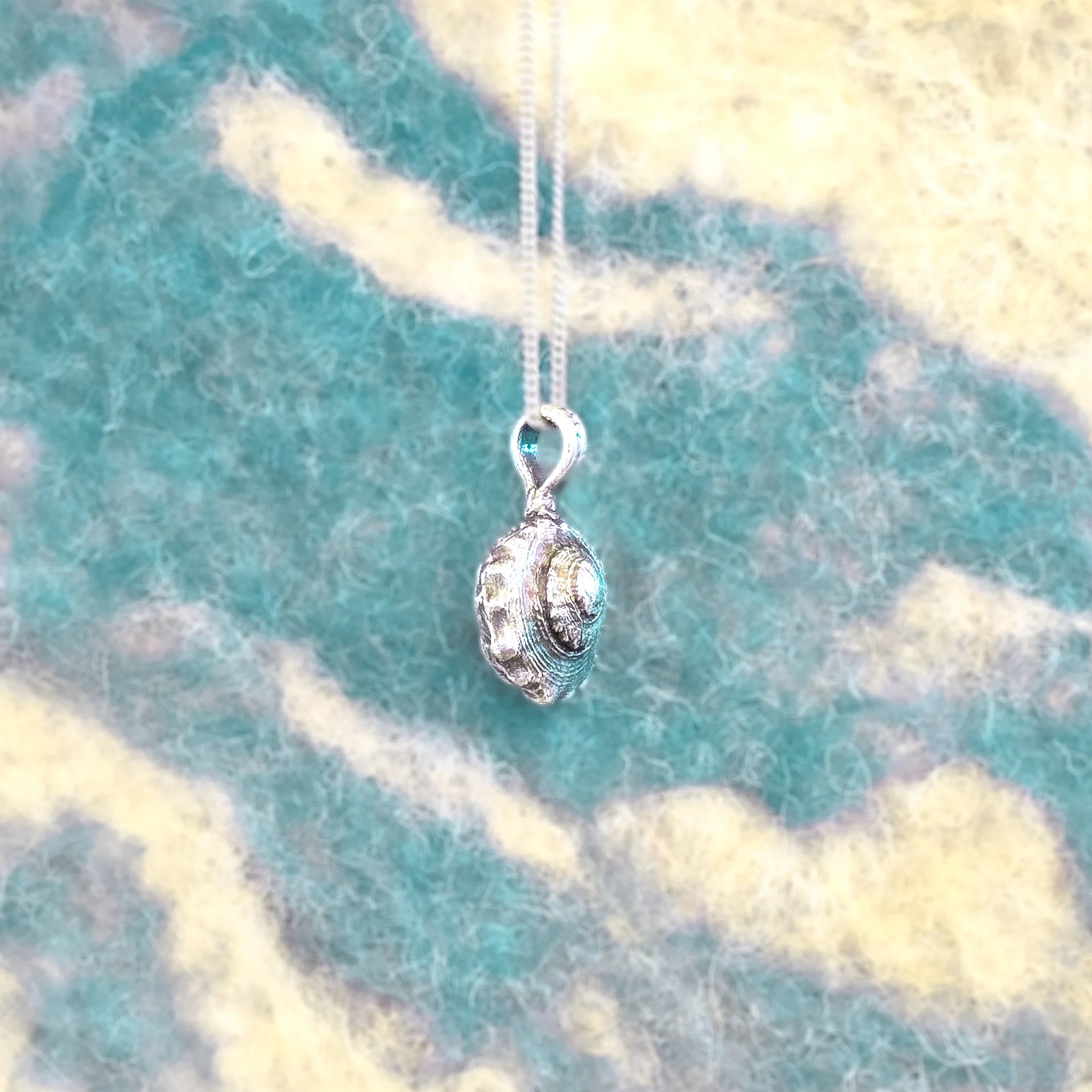 Fine silver textured shell pendant with concentric ridged rings, worn on a silver chain against bare skin