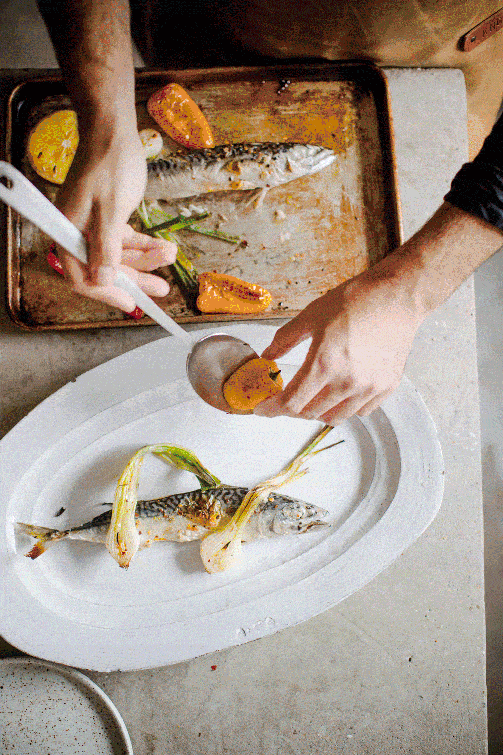 Person roasting whole fish with lemon and bell peppers on a white plate, cooking preparation scene.