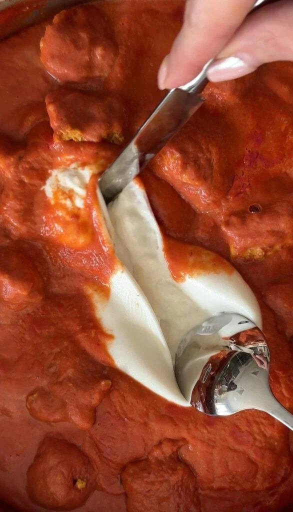 A person slicing a large meat lasagna with a metal spatula, showing layers of pasta, cheese, and tomato sauce.