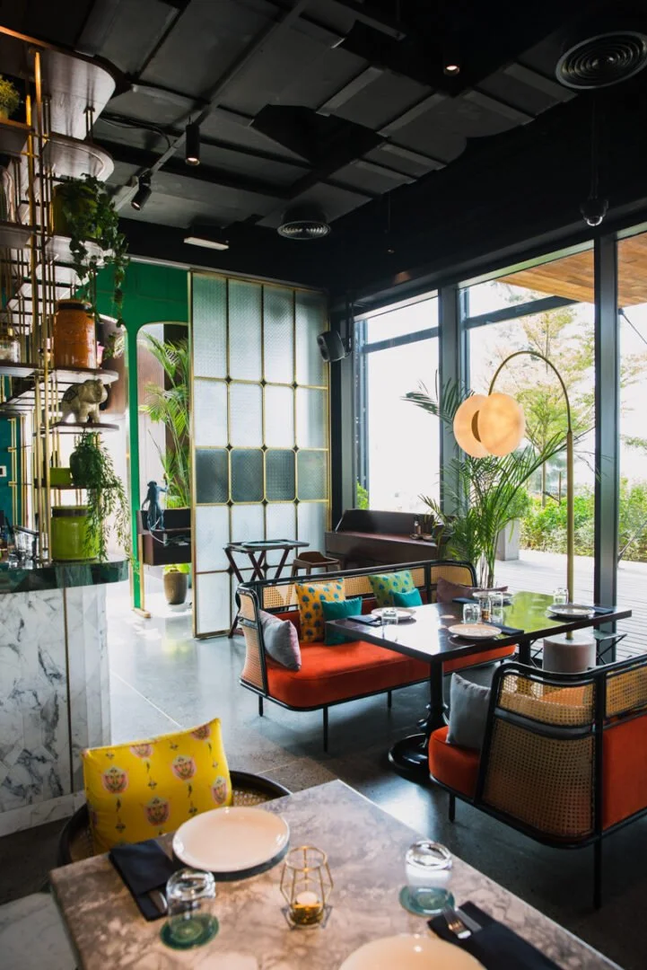 Interior of a modern restaurant with colorful seating, large windows, and green plants.