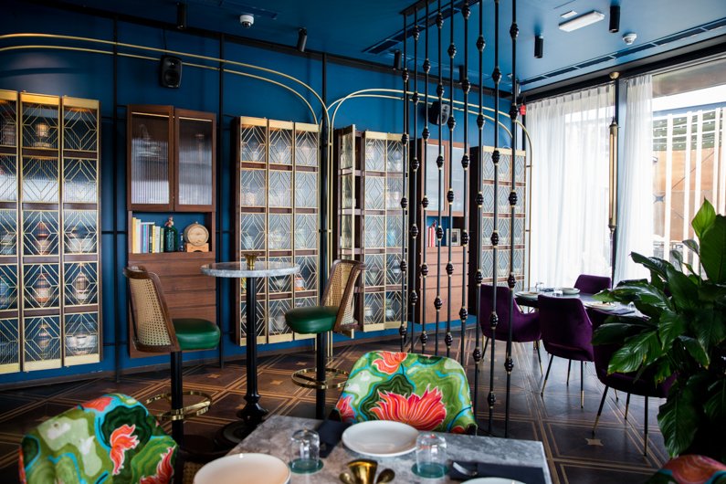 Interior of Masti restaurant or cafe with blue walls, gold accents, colorful chairs and a small round tables