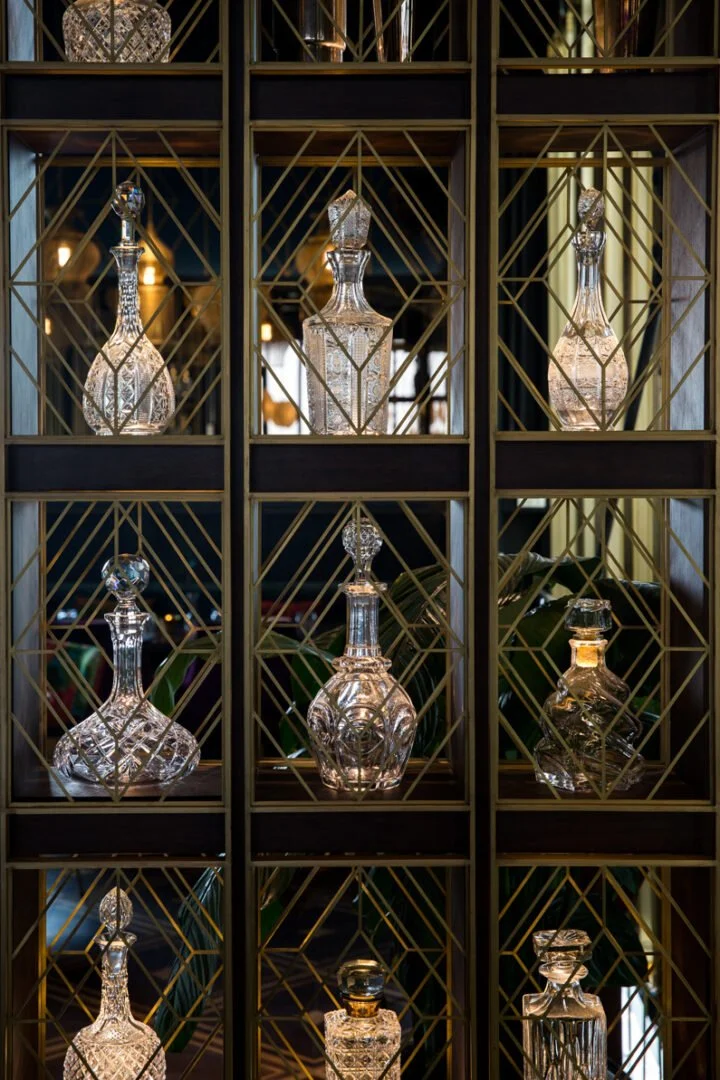 Decorative glass decanters on a gold metal grid shelving unit at Masti restaurant
