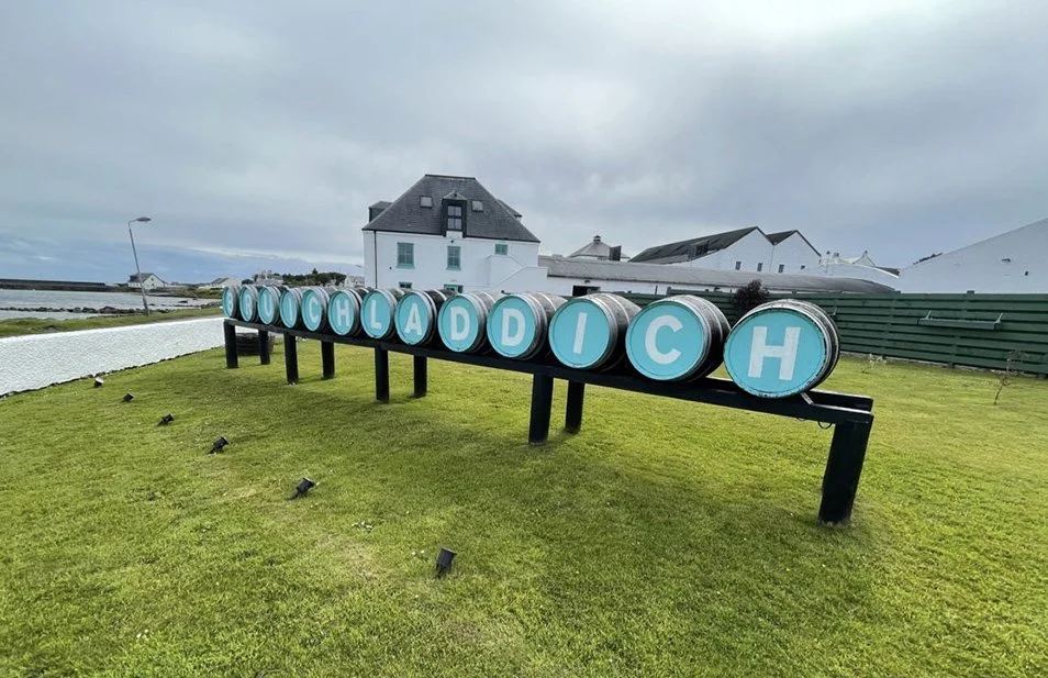 A display of barrel-shaped signs spelling 'COACH LADY H' on a grassy area near white houses