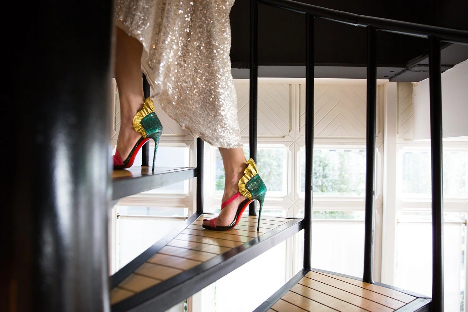 A person wearing sparkly gold dress and multicolored high heel shoes climbing a wooden staircase in a well-lit room.