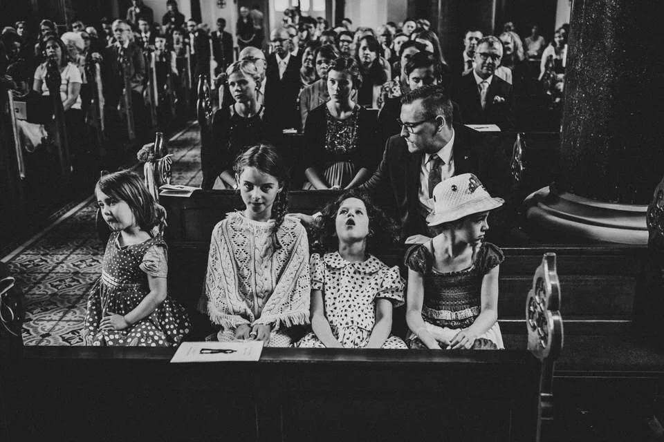 Schwarz-weiß-Bild von einer Kirche mit Menschen im Gottesdienst, vor allem Kinder im Vordergrund, die auf den Bänken sitzen.