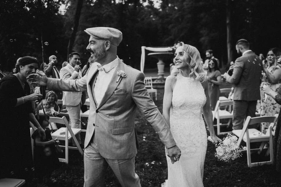 Ein Brautpaar bei ihrer Trauung im Freien, umgeben von Freunden und Familie, lachend und glücklich, während sie sich die Hände halten.