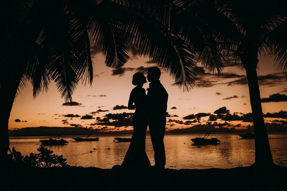 Paare, die sich bei Sonnenuntergang an einem Strand unter Palmen küssen.