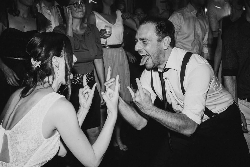 Paar beim Feiern, lachen und spielen auf einer Party, im Hintergrund andere Gäste, schwarz-weiß Foto.