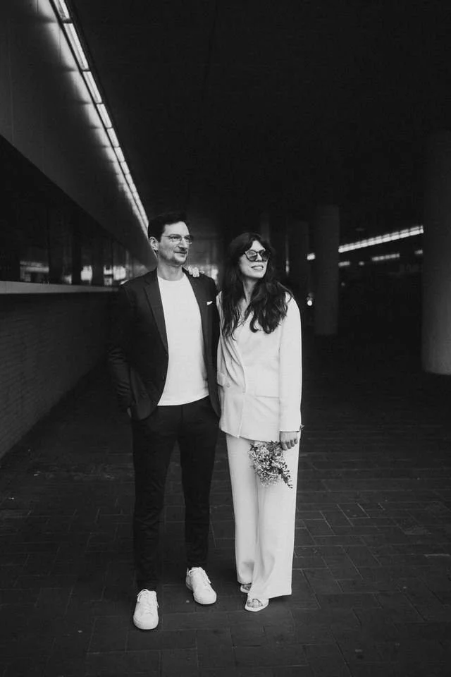 Zwei Menschen, ein Mann und eine Frau, stehen in einem dunklen, modernen Raum, der vermutlich eine U-Bahn-Station oder ein Tunnel ist.