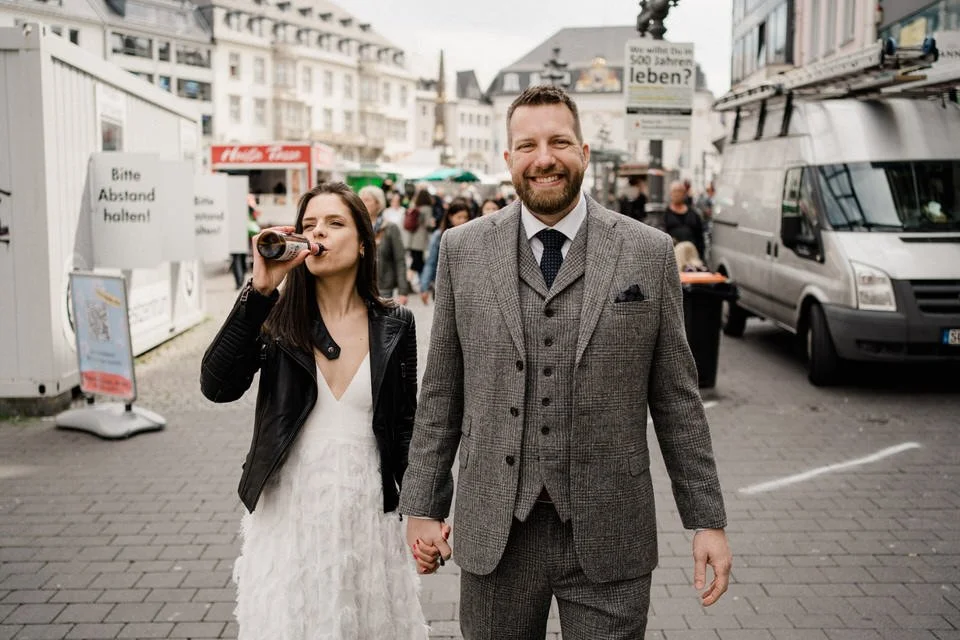Ein glückliches Paar läuft Händchen haltend auf einer belebten Stadtstraße, im Hintergrund sind Menschen, Fahrzeuge und Geschäfte zu sehen.