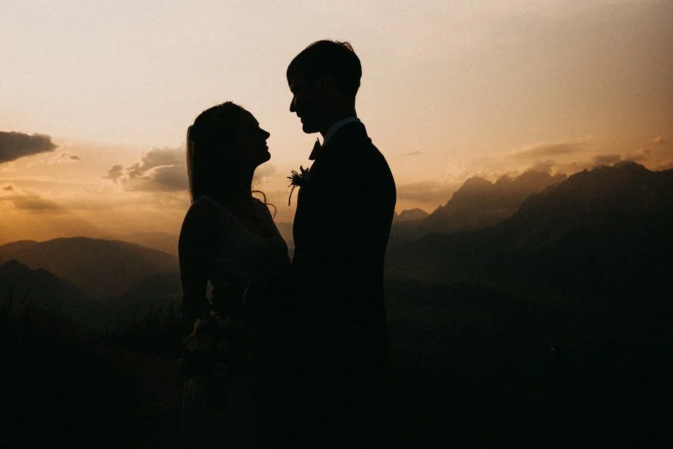 Silhouette eines verliebten Paares vor Sonnenuntergang mit Bergen im Hintergrund.