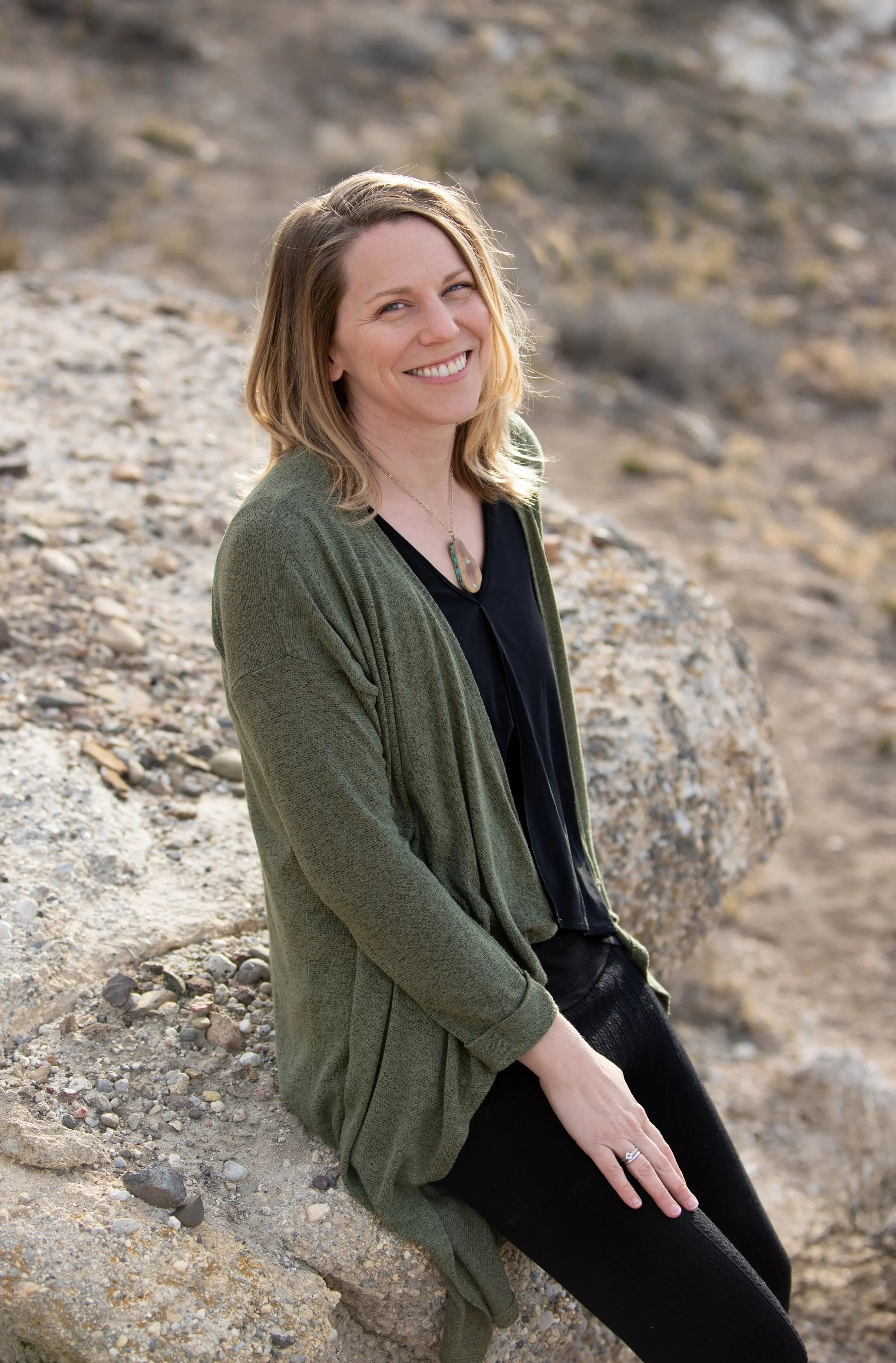 Alicia Langton- EcoloGIS lead ecologist smiling while sitting on a rock.