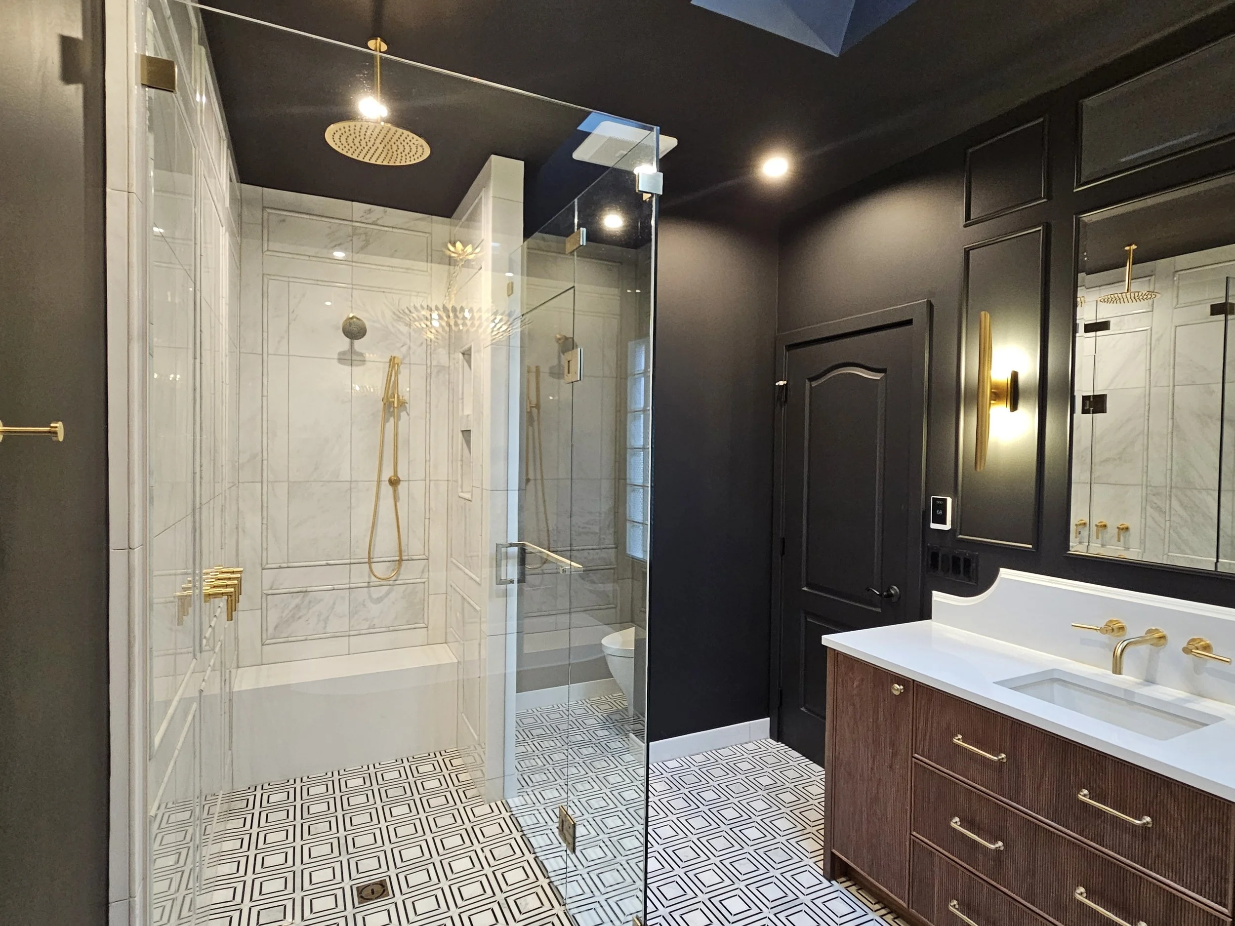 "A luxury modern bathroom remodel featuring a seamless glass shower, gold rain shower head, and decorative floor tile—engineered for both high-end style and long-term safety by M1 Custom Bathrooms."