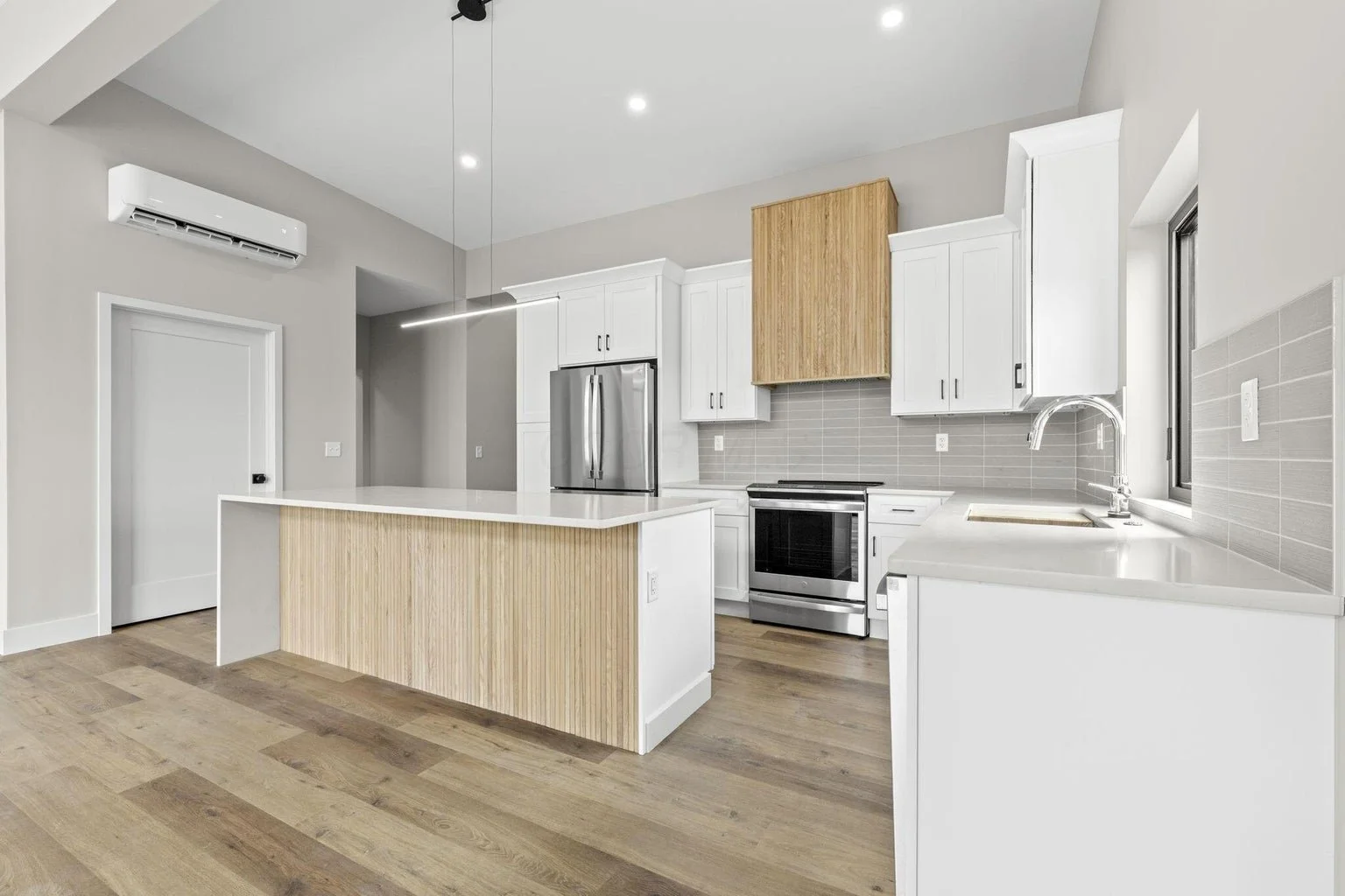 Modern kitchen with white cabinets, stainless steel appliances, a wooden island, and a wood-colored range hood. Light gray tile backsplash and hardwood flooring.