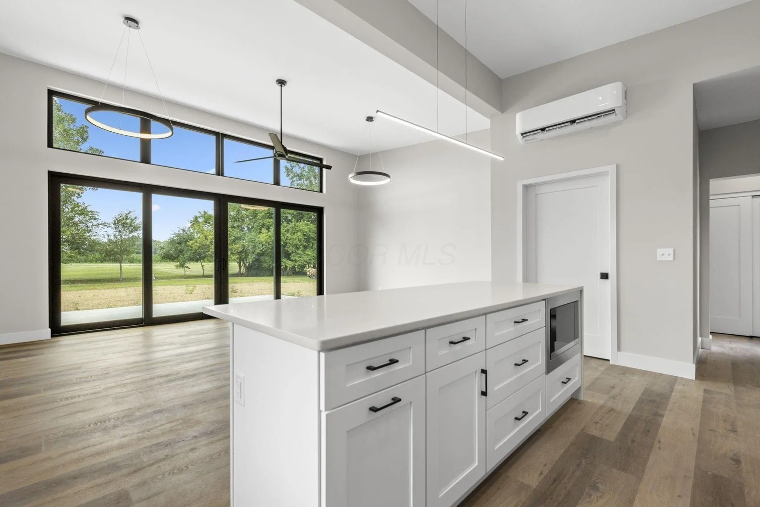 Modern kitchen with white cabinets, a white countertop island, large front window, and minimalist lighting fixtures.