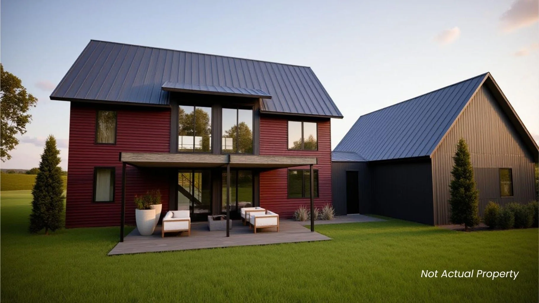 Modern two-story house with red and black siding, large windows, a wooden deck with outdoor seating, surrounded by a well-manicured lawn and trees, under a clear sky.
