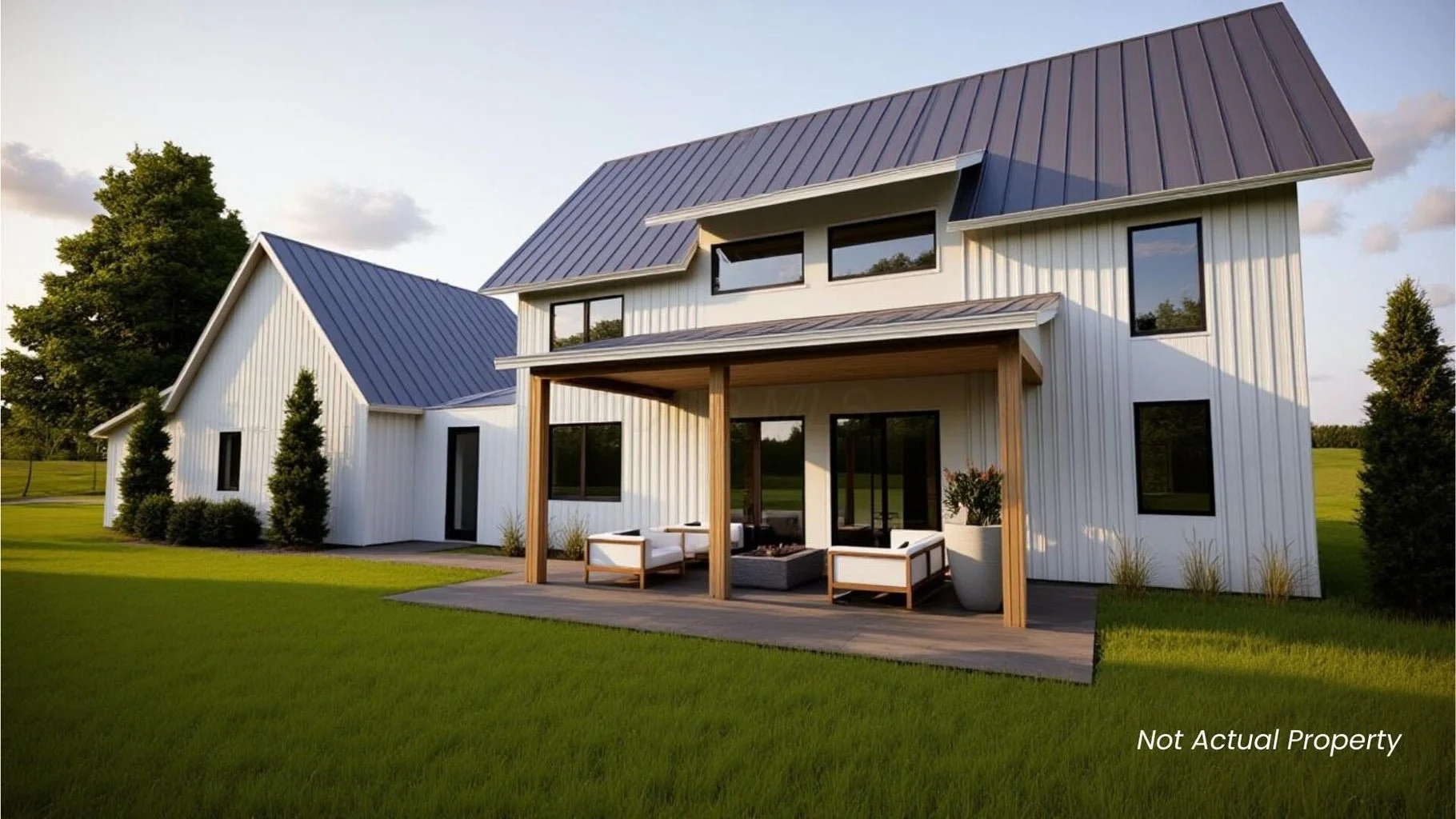 Modern white house with metal roof, large windows, and outdoor seating area on a wooden deck, surrounded by green lawn and trees.
