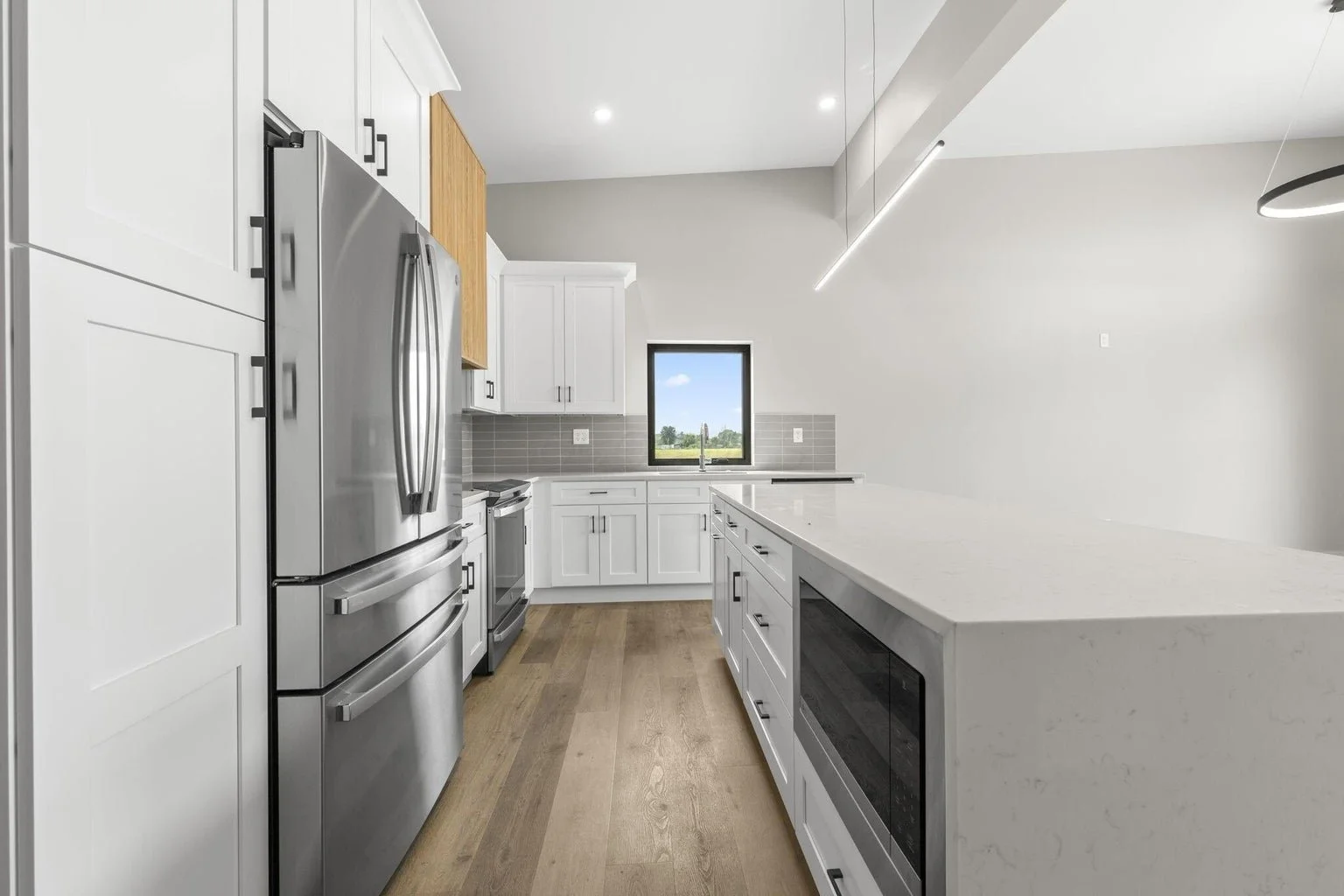 Modern kitchen with white cabinets, stainless steel refrigerator and oven, gray tile backsplash, wooden accents, and hardwood floors.