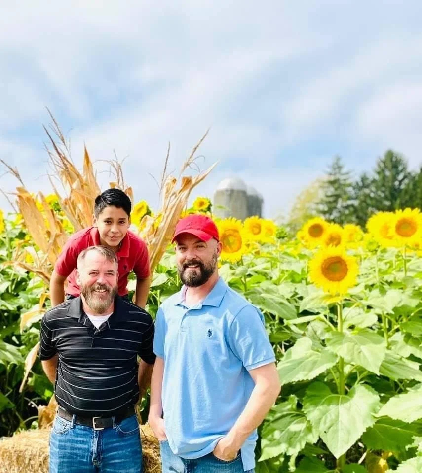 An image of a happy queer family in a field of sunflowers.