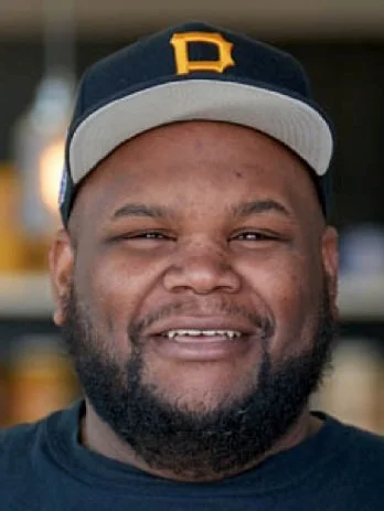 A picture of Sammy McDowell, a smiling black man wearing a baseball cap and black t-shirt.
