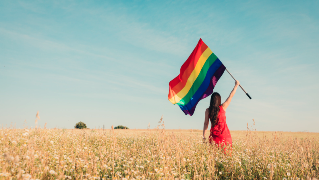 Woman holding a rainbow flag in a field