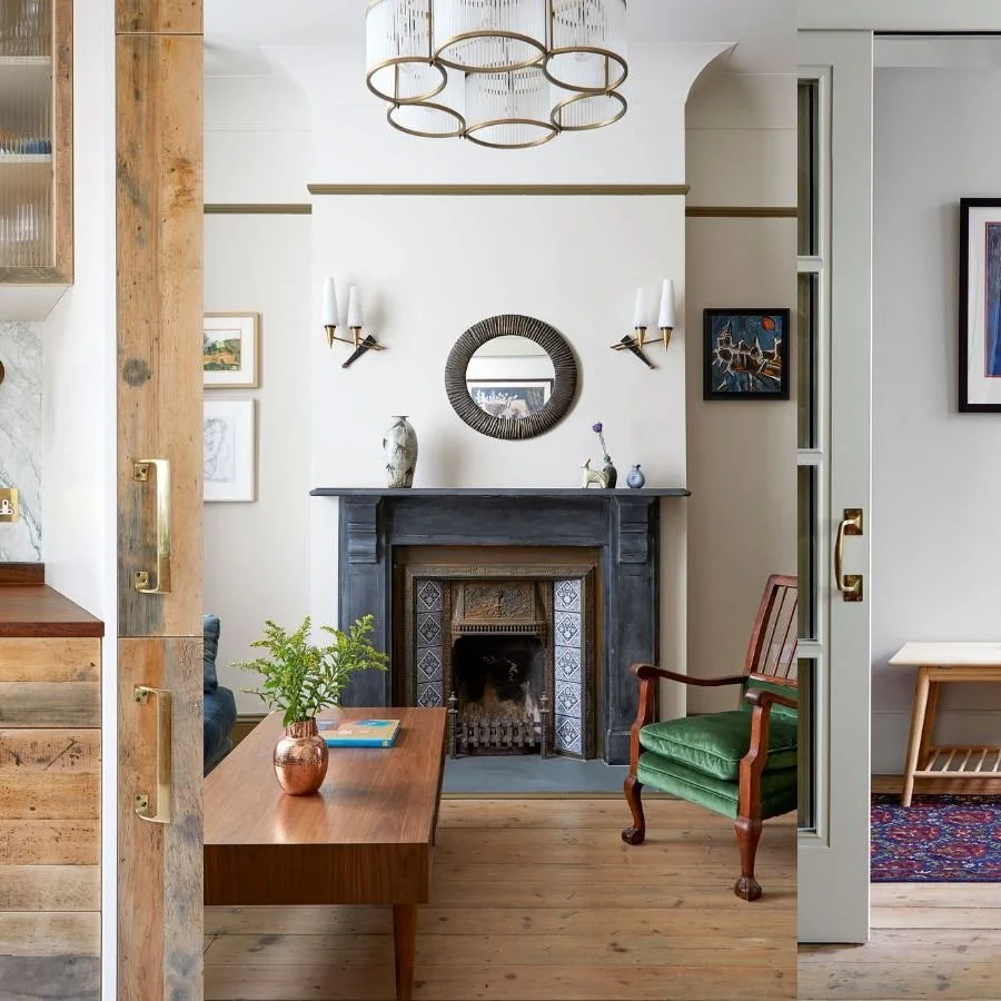 Living room with a black fireplace, a round mirror above it, two wall sconces, a wooden side table, a green armchair, and a round chandelier.