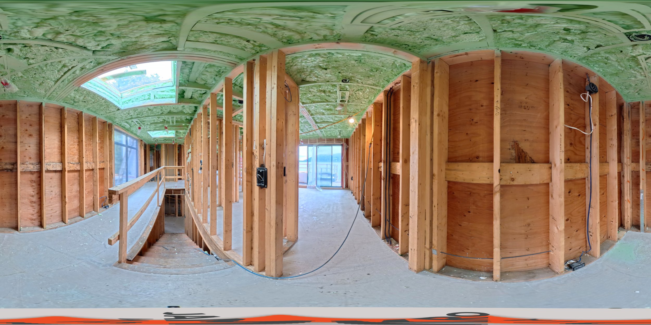 Interior view of a house under construction showing wooden framing, walls, and ceiling insulation, with openings for windows and a staircase.